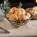 A Clipper Mill chrome plated iron round basket filled with bread on a table.