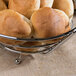 A close-up of a Clipper Mill chrome plated iron round basket filled with bread rolls.