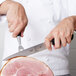 A person using a Mercer Genesis Forged Carving Knife to slice a ham.