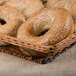 A Clipper Mill honey wicker wire basket with a bagel topped with sesame seeds.