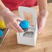 A person in gloves holding a cupcake in a Baker's Mark cupcake box.