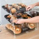 A woman putting a bag of muffins into a large clear bakery display case with front doors.