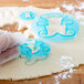 A person using a blue Ateco teddy bear cookie cutter to cut out a cookie.