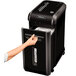 A hand is putting paper into a Fellowes Powershred 99Ms paper shredder.