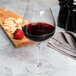 A Chef & Sommelier Cabernet wine glass filled with red wine next to a cutting board with crackers and strawberries.