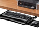 A Fellowes black underdesk keyboard drawer holding a keyboard and mouse under a desk.