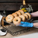 A person in blue gloves placing a Clipper Mill clear plastic liner in a basket of bagels.