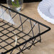 A clear plastic basket liner in a black wire basket with a glass vase and white plates.