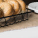 A Clipper Mill clear plastic basket liner holding a bagel in a food display basket on a bakery counter.