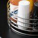 A Clipper Mill stainless steel round condiment caddy filled with condiments in a metal basket with a card holder.