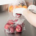 A person wearing gloves putting red apples in an Inteplast plastic food bag.