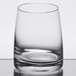 A Stolzle old fashioned glass with a small amount of liquid on a white background.
