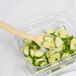 A beige Cambro Camwear salad bar spoon in a bowl of cucumbers.