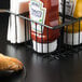 A black Clipper Mill 4-compartment condiment caddy with condiments and napkins on a black surface.