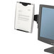 A Fellowes black plastic monitor mount with a paper clipped to a computer screen.