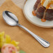 An Acopa Edgeworth stainless steel dinner/dessert spoon on a plate with a cake on it.