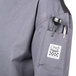 A close-up of a Chef Revival gray long sleeve chef jacket with a pocket and pen holder.