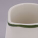 A close up of a Tuxton eggshell white china creamer with a green band.