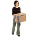 A woman holding a Banker's Box cardboard moving box with a smile on her face.