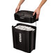 A person holding a black Fellowes Powershred 11C paper shredder with shredded paper.