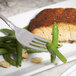 A Bon Chef stainless steel dinner fork on a plate with green beans and fish.