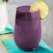 A Stolzle purple stemless wine glass with a lemon wedge in purple liquid.