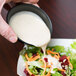 A person pouring a black Solo sauce cup of white sauce onto a salad.