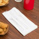 A white napkin rolled around clear plastic cutlery with a Hoffmaster Damask Linen-Like design.
