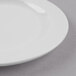 A close up of a Libbey bright white porcelain plate with a medium rim on a gray surface.