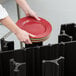 A person holding a black metal Cambro dish caddy holding red plates.