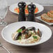 A Libbey bright white porcelain bowl with pasta and mussels on a table.