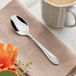 An Acopa Monaca stainless steel teaspoon on a napkin next to a mug of coffee.