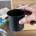 A person holding a black cup with white substance on their finger.
