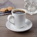 A Libbey bright white porcelain saucer with a cup of coffee on it and a glass of water.