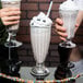 A hand holding a Libbey soda glass filled with a milkshake and topped with whipped cream and a cherry.