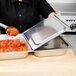 A person using a Vollrath hinged cover on a metal tray of food.