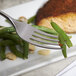 A Bon Chef stainless steel dinner fork on a plate with green beans and a piece of meat.