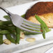 A Bon Chef Como dinner fork spearing a piece of fish and green beans on a plate.