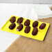 A chocolate covered donut on a yellow Tablecraft rectangular cooling platter.