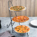 A Clipper Mill by GET black powder coated iron three-tier pizza stand holding pizzas on a table.