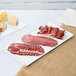 A Tablecraft white cast aluminum rectangular cooling platter with meat and cheese on it.