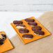 An orange Tablecraft cast aluminum rectangular cooling platter with chocolate covered donuts on a table.