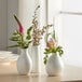 Three white Acopa porcelain bulb bud vases with flowers in them.