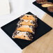 A Tablecraft midnight black cast aluminum rectangular cooling platter with blue speckles holding chocolate covered pastries on a table.