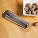 A Fox Run stainless steel nutmeg grater grating nutmeg over a bowl of nuts.