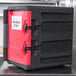 A black Metro Mightylite insulated food pan carrier with a red door.