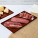 Two brown Tablecraft cast aluminum rectangular trays holding meat and cheese.