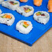 A Tablecraft blue speckled rectangular cast aluminum cooling platter with sushi rolls on a blue surface.