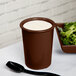 A brown Tablecraft cast aluminum salad dressing crock filled with white liquid.