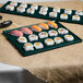 Two Tablecraft hunter green and white speckled cast aluminum rectangular cooling platters with sushi on a table.